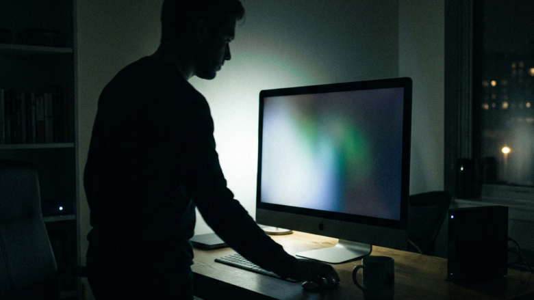 Silhouette of a person working on a desktop computer in a dark room